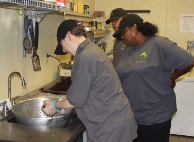 Deborah Swetz of Marrakech, left, wrings out a handful of gracilaria before placing it on a rack for dehydration as Debra Watson, center, employment specialist at Marrakech Inc., looks on.