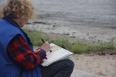 Mary Horrigan of Marlborough painted with water colors near a small sandy beach next the the Marine Sciences Building.