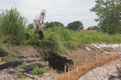 University of Delaware student Sam Koeck shovels compost over a coconut fiber core log at the Stratford Point site where he is working for the summer.