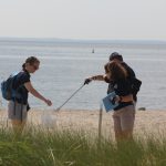 Lisa Jarosik, right, a dive volunteer at the Maritime Aquarium, places trash collected on the beach at Sherwood Island in a bucket held by Bridget Cevero, education manager at the aquarium. Among the items the pair picked up were flip-flops, several tubes of lip balm, large pieces of confetti and a cement trowel.