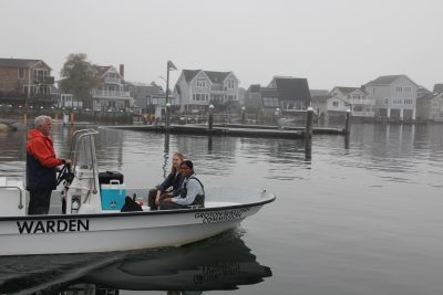 Ted Rathjen, senior shellfish warden for Groton, steers the boat as Kaitlyn Campbell, post doctoral student in the Brandt Lab at UConn, and Anika Agrawal, doctoral student in the lab, prepare to collect oysters and mussels to test for PFAS in shellfish tissue in an earlier research project led by Christopher Perkins, who was chosen for one of the four CECs project research awards.