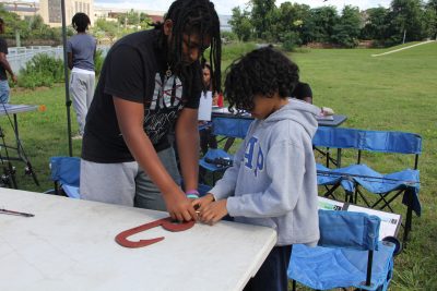 Matthew Roscoe, left, an employee of the New Haven-based nonprofit group Community Placemaking Engagement Network (CPEN), teaches eight-year-old Ja'terrie James how to tie a knot.