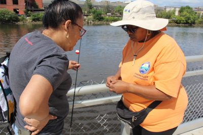 CT DEEP Fishing Coach Loreen Lawrence, right, shows Elena Padin how to bait a hook.