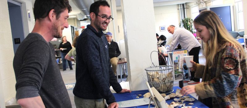 CTSG assistant extension educators Mike Gilman, left, and Zach Gordon, center, talk with UConn Avery Point student Cameron Salas about shell recycling and different types of shellfish in Long Island Sound at the EcoHusky Earth Day fair April 21 in the Avery Point library.